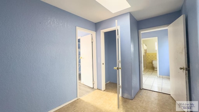 hall featuring light tile patterned flooring and a skylight