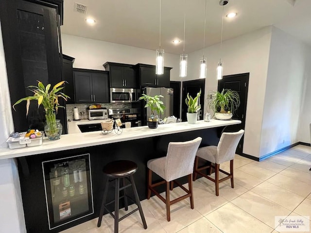 kitchen with a kitchen bar, decorative light fixtures, stainless steel appliances, and beverage cooler