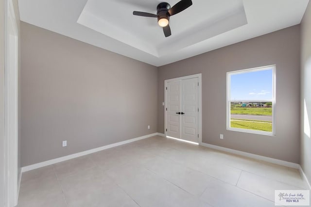 tiled spare room featuring a raised ceiling and ceiling fan