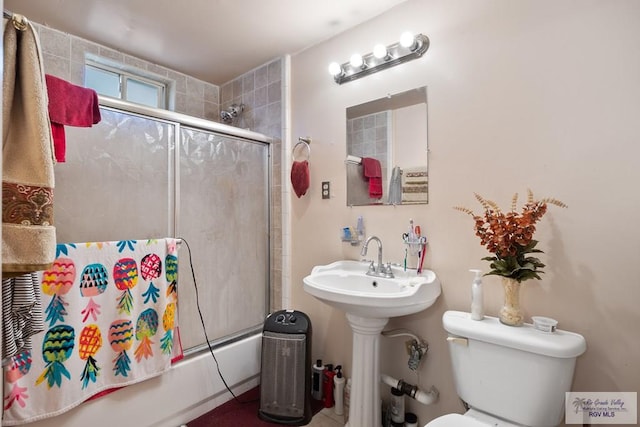 bathroom featuring toilet and bath / shower combo with glass door