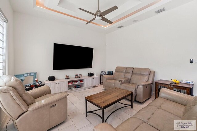 tiled living room featuring a tray ceiling, plenty of natural light, and ceiling fan