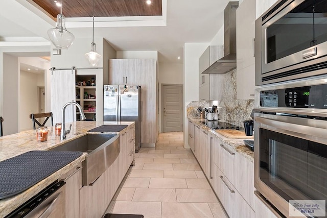 kitchen with sink, wall chimney range hood, light stone counters, decorative backsplash, and appliances with stainless steel finishes