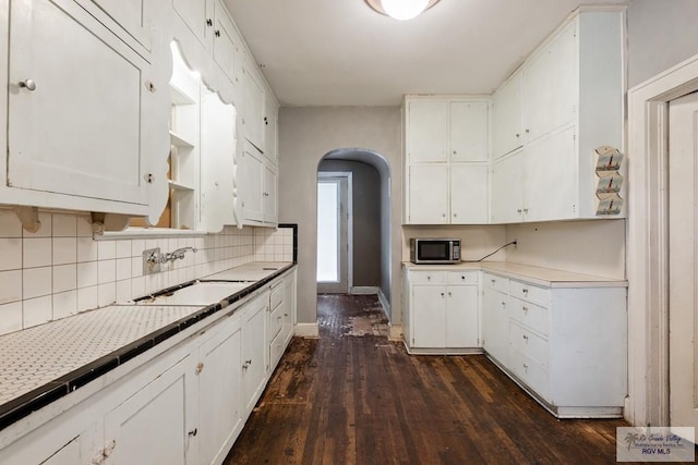 kitchen with tasteful backsplash, arched walkways, white cabinets, stainless steel microwave, and a sink