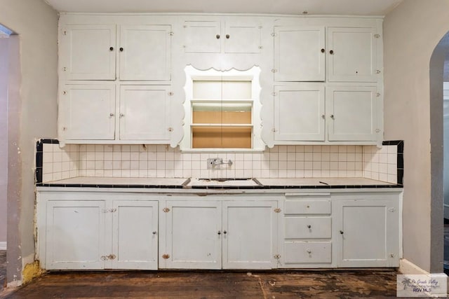 kitchen with white cabinetry, tile counters, arched walkways, and decorative backsplash