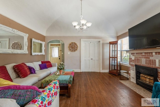 living room featuring an inviting chandelier, a brick fireplace, vaulted ceiling, wood finished floors, and baseboards