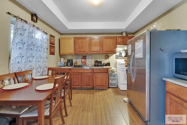 kitchen with light wood-style flooring, appliances with stainless steel finishes, brown cabinets, a tray ceiling, and light countertops