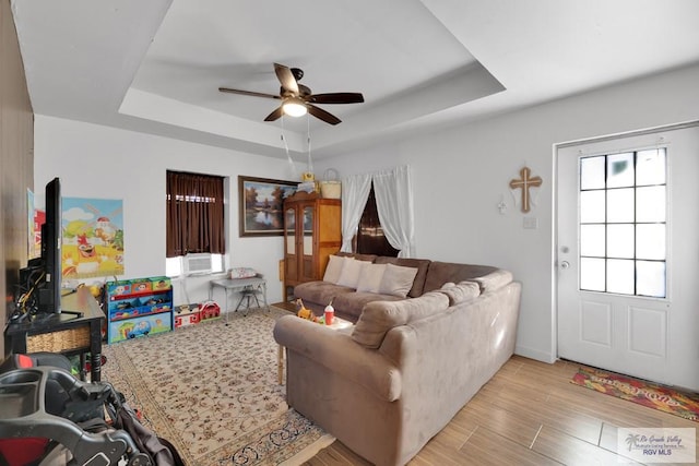 living room featuring light wood-type flooring, a raised ceiling, and a ceiling fan