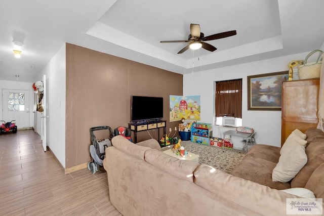 living area with light wood finished floors, a tray ceiling, and a ceiling fan