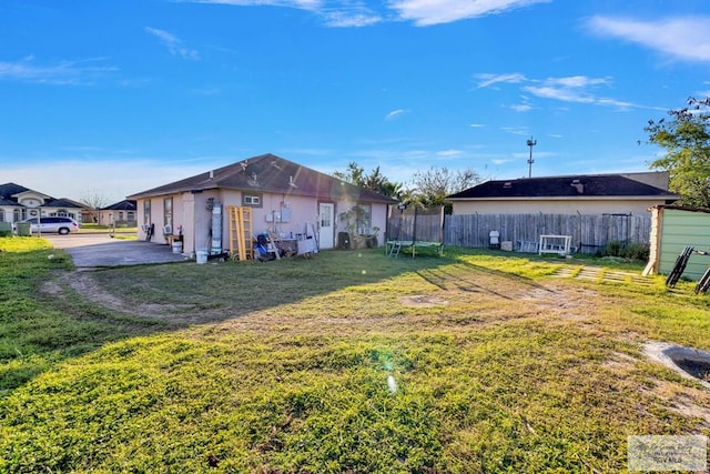 back of property with a trampoline, fence, and a lawn