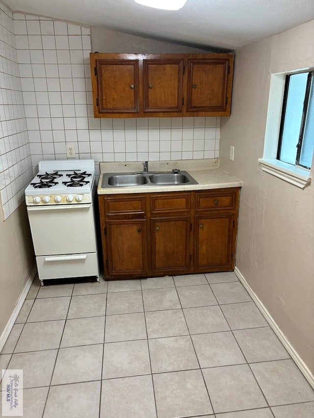 kitchen with sink, vaulted ceiling, white range with gas cooktop, light tile patterned floors, and tile walls