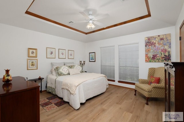 bedroom with a tray ceiling, ceiling fan, and light wood finished floors