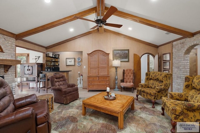 living area featuring visible vents, arched walkways, a ceiling fan, a fireplace, and vaulted ceiling with beams
