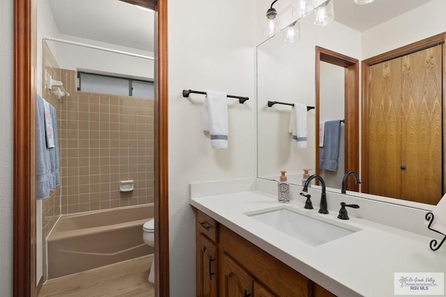 bathroom with toilet, wood finished floors, vanity, and shower / washtub combination
