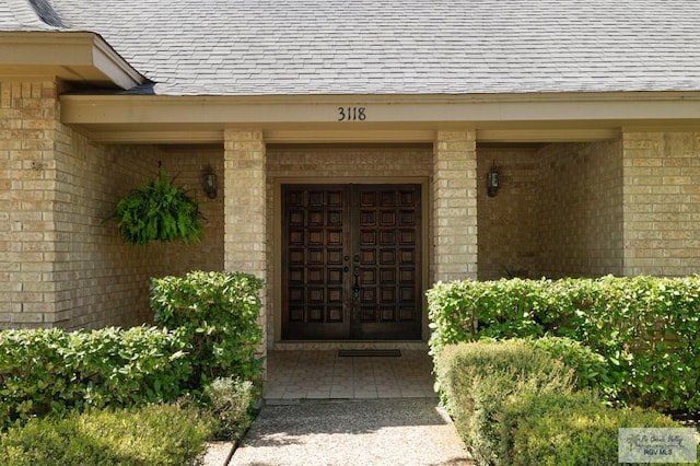 property entrance featuring brick siding and a shingled roof
