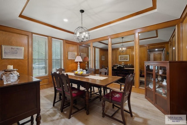 dining area with ornamental molding, light wood-type flooring, a chandelier, wooden walls, and a tray ceiling