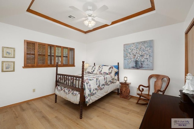 bedroom featuring light wood-type flooring, a raised ceiling, baseboards, and a ceiling fan
