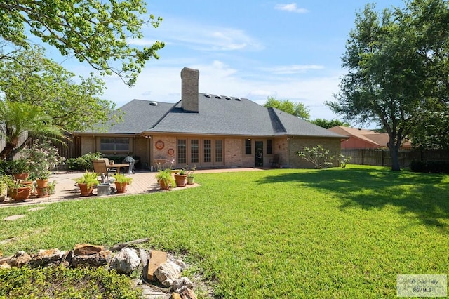 rear view of property with a yard, a patio, fence, brick siding, and a chimney