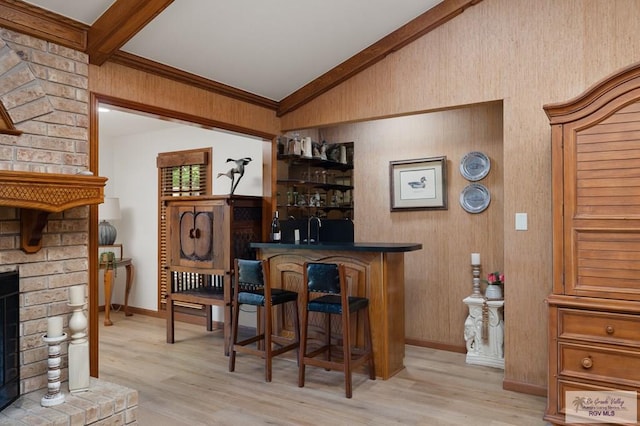 bar with a fireplace, a dry bar, vaulted ceiling with beams, light wood finished floors, and baseboards