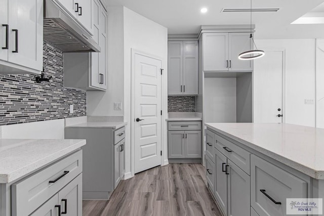 9718 Alexis Ave, Harlingen, TX 78550 - kitchen with backsplash, light stone countertops, wood finished floors, gray cabinetry, and under cabinet range hood