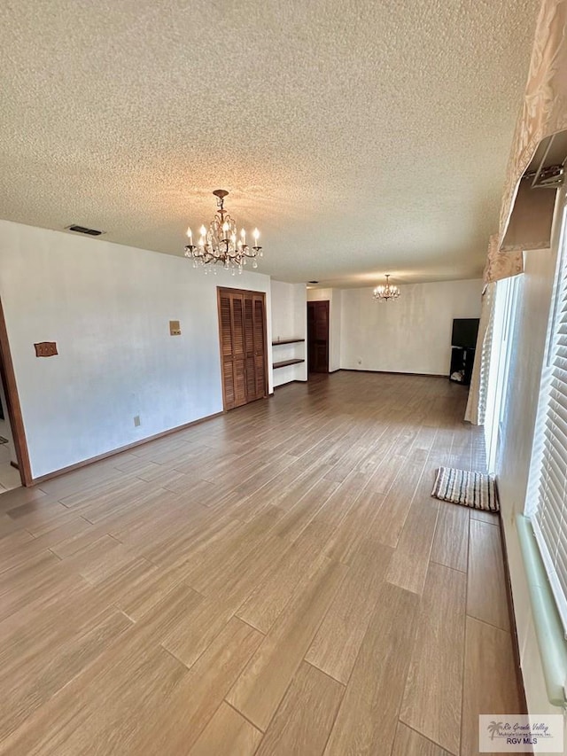 unfurnished living room with a notable chandelier, a textured ceiling, and light hardwood / wood-style flooring