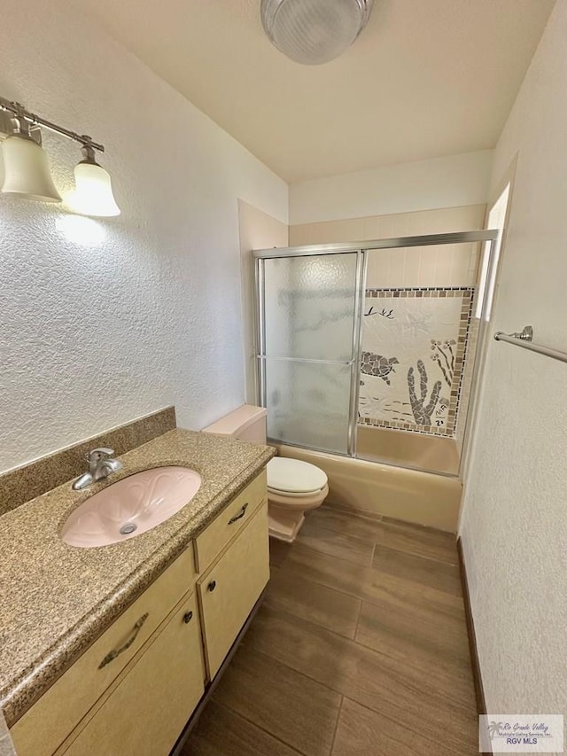 full bathroom featuring hardwood / wood-style flooring, vanity, toilet, and shower / bath combination with glass door