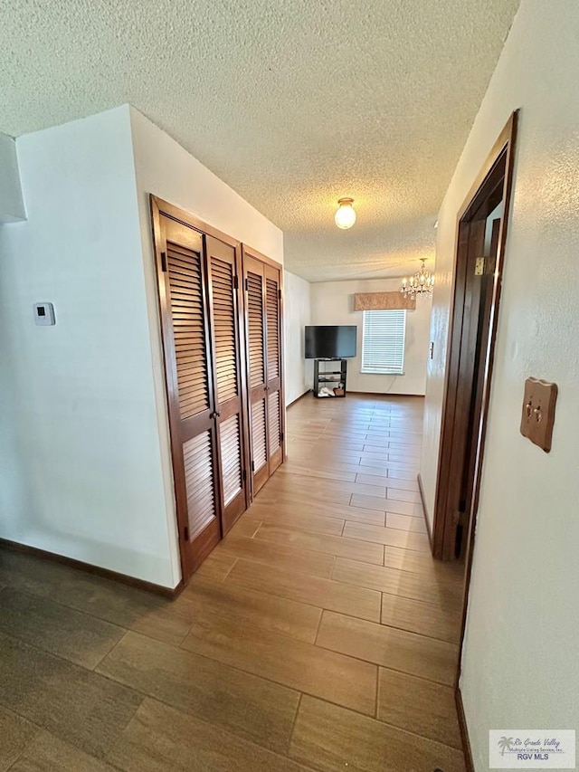 corridor featuring a textured ceiling, hardwood / wood-style flooring, and a notable chandelier