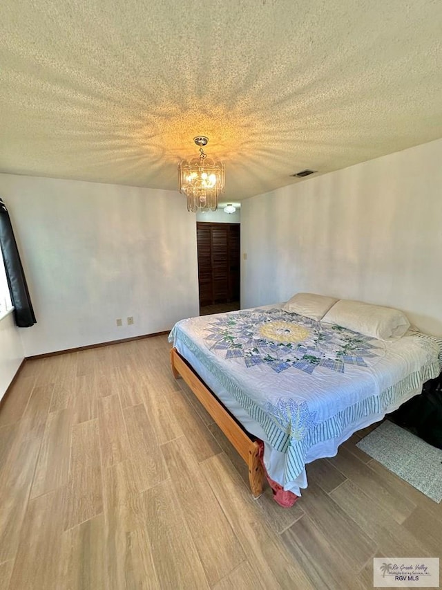 bedroom featuring a chandelier, a textured ceiling, and light wood-type flooring