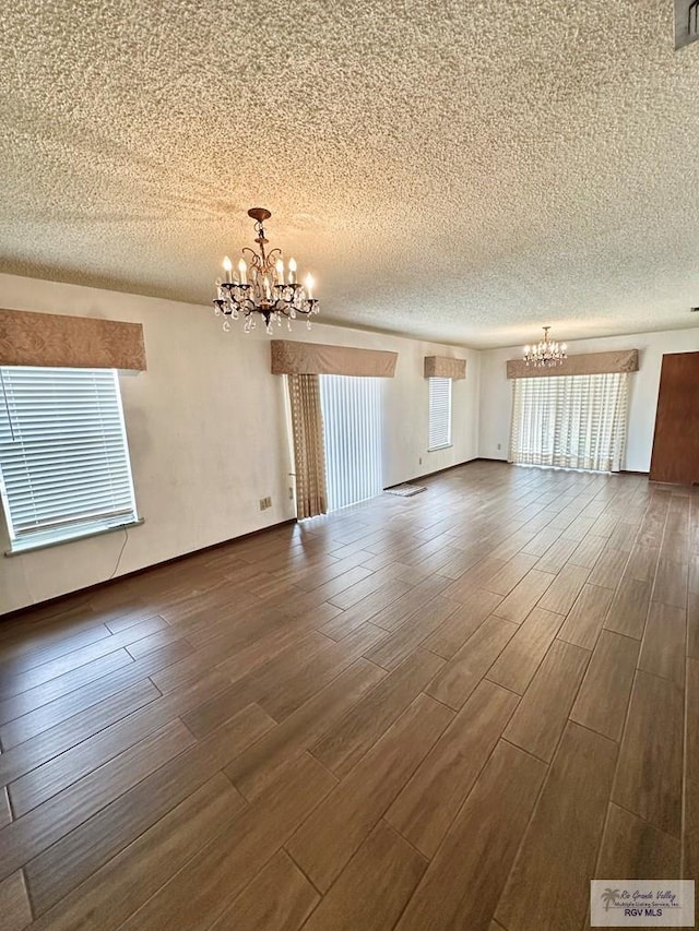 unfurnished room featuring a notable chandelier, dark hardwood / wood-style flooring, and a textured ceiling