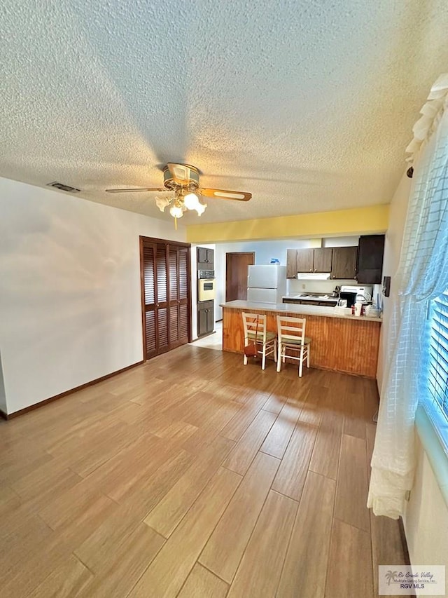 kitchen with a kitchen breakfast bar, kitchen peninsula, a textured ceiling, white appliances, and light wood-type flooring