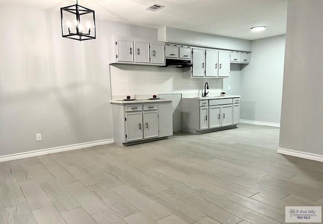 kitchen featuring visible vents, a sink, under cabinet range hood, tasteful backsplash, and light wood-type flooring