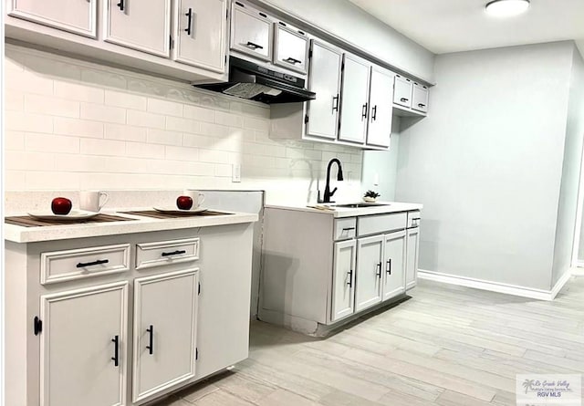 kitchen featuring light countertops, backsplash, under cabinet range hood, and a sink