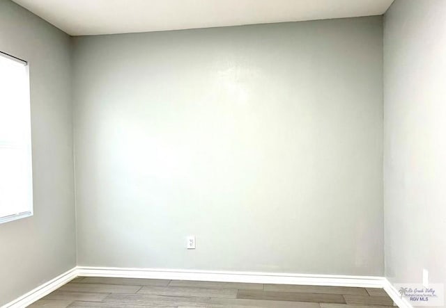 spare room with baseboards and wood finished floors