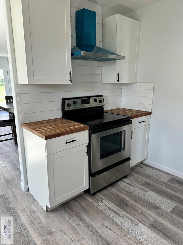 kitchen featuring butcher block countertops, electric stove, wall chimney exhaust hood, and light hardwood / wood-style floors