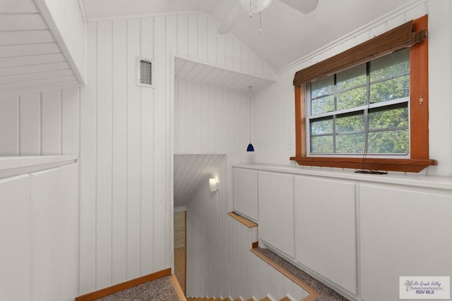 stairway with wooden walls, ceiling fan, and lofted ceiling