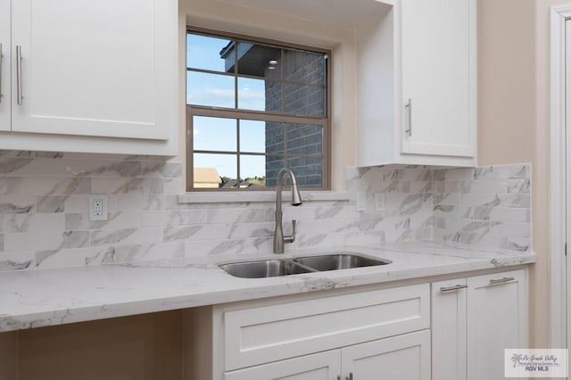 kitchen featuring tasteful backsplash, sink, white cabinetry, and light stone counters