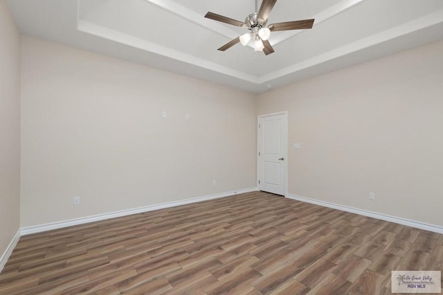 empty room with wood-type flooring, ceiling fan, and a tray ceiling