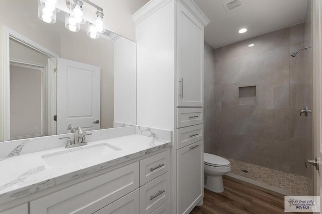 bathroom featuring wood-type flooring, toilet, vanity, and a tile shower