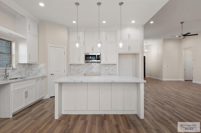 kitchen featuring white cabinetry, decorative light fixtures, a center island, and sink