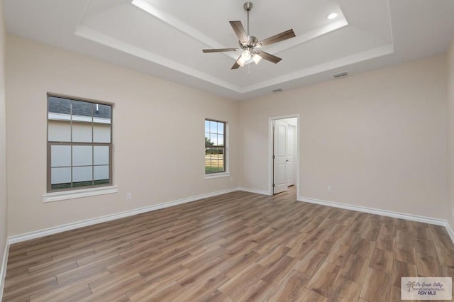 unfurnished room with a raised ceiling, ceiling fan, and light wood-type flooring