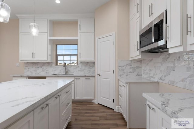 kitchen with dark wood-type flooring, sink, light stone counters, pendant lighting, and white cabinets