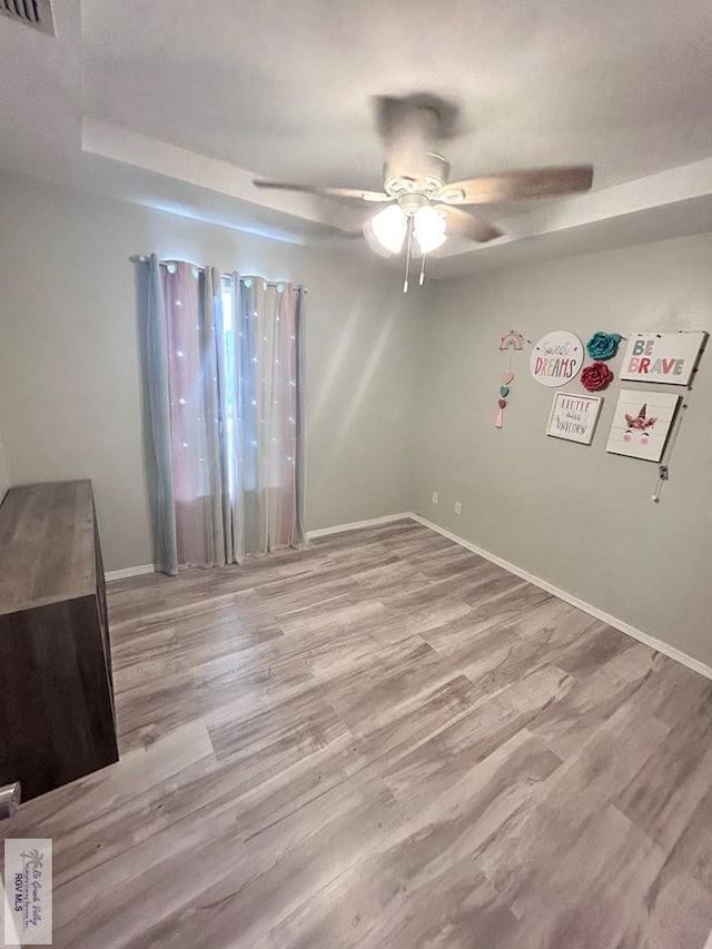 interior space featuring a raised ceiling, light hardwood / wood-style floors, and ceiling fan