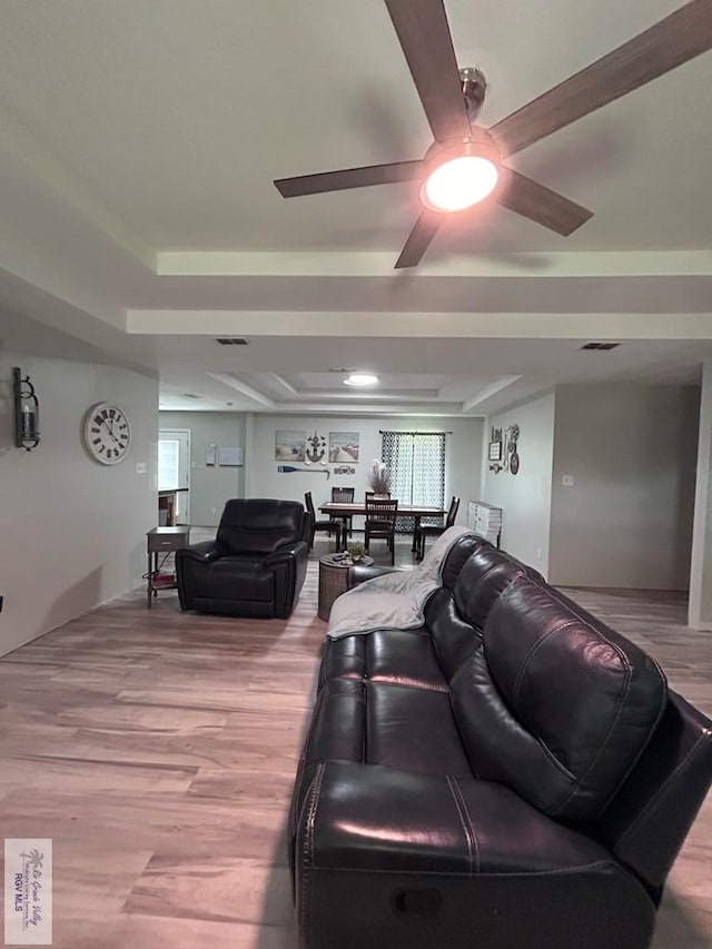 living room featuring a tray ceiling, light wood-type flooring, and ceiling fan