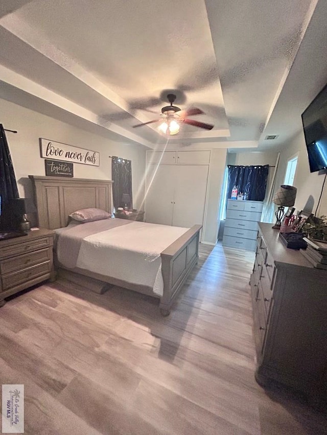 bedroom featuring ceiling fan, light wood-type flooring, a raised ceiling, and a textured ceiling