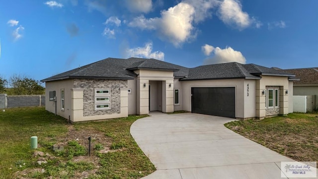 prairie-style home with a garage, fence, concrete driveway, stone siding, and a front lawn