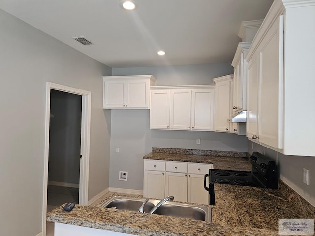 kitchen with dark stone countertops, electric range, sink, and white cabinets