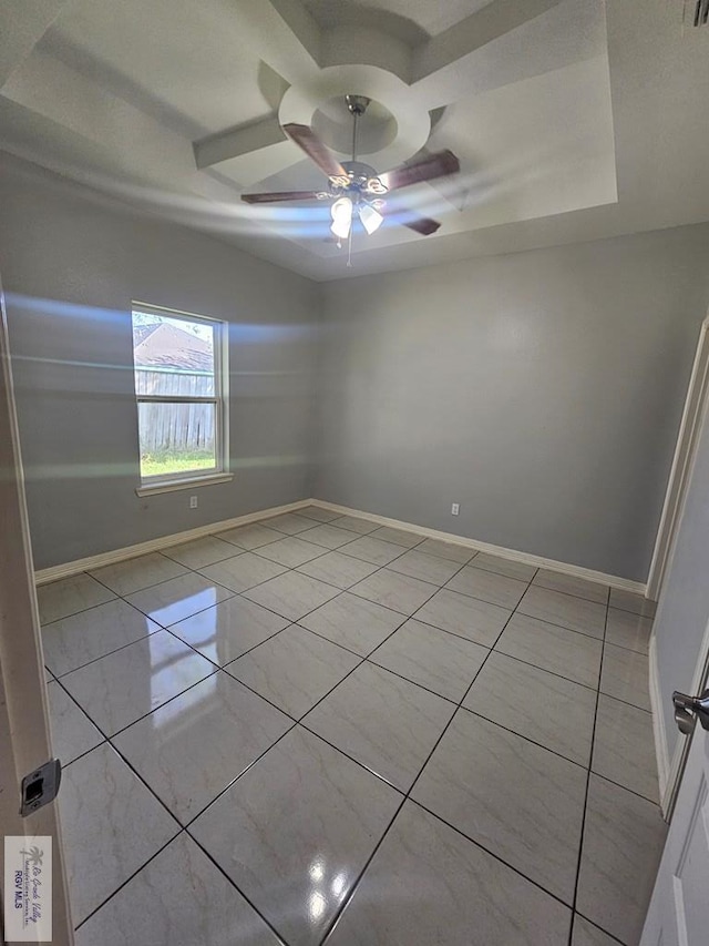 tiled spare room featuring a tray ceiling and ceiling fan