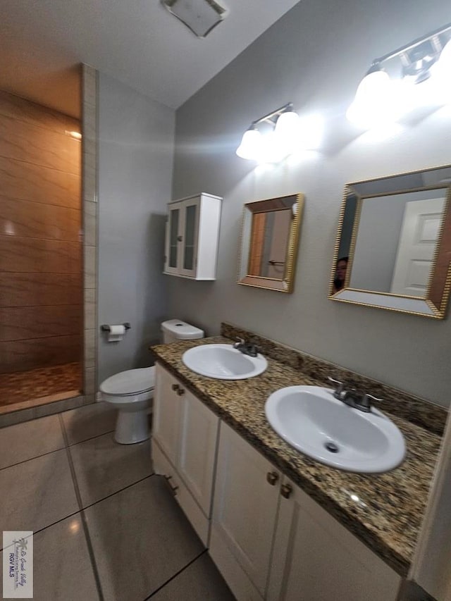 bathroom featuring tile patterned flooring, a tile shower, vanity, and toilet