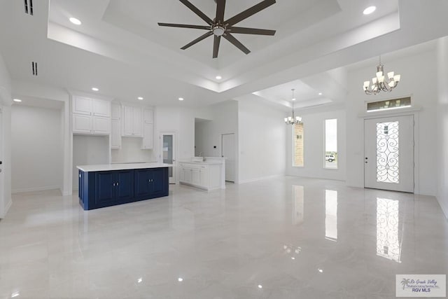 unfurnished living room with ceiling fan with notable chandelier and a tray ceiling