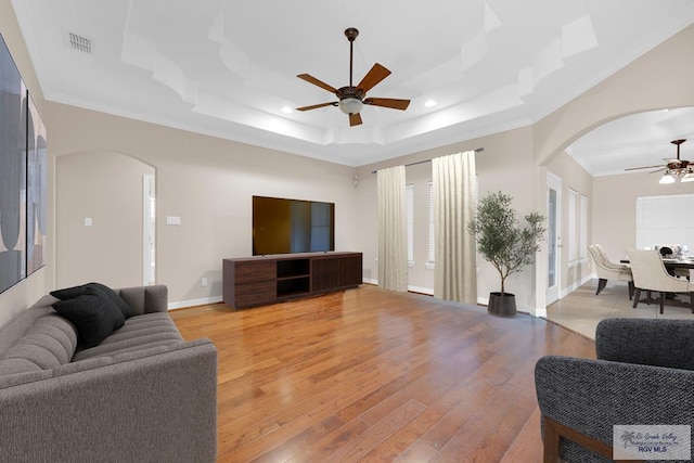 living room featuring arched walkways, a raised ceiling, visible vents, and ceiling fan