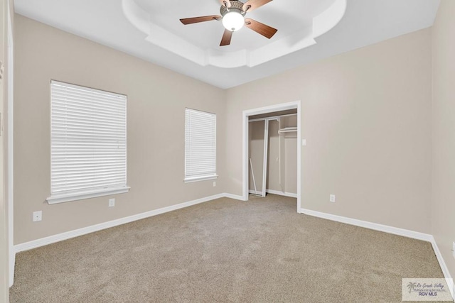 unfurnished bedroom featuring a closet, a raised ceiling, light colored carpet, and baseboards